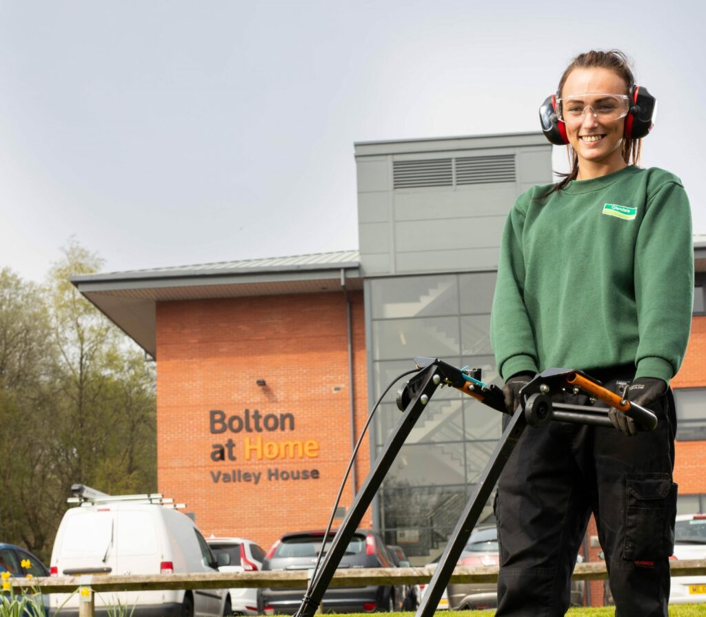 Bolton at Home; Futr AI, gardener lady with lawnmower, in front of branded building